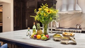 Un îlot de cuisine orné d’un panier de fruits, d’une bouteille de liqueur, d’un ananas et d’un vase de fleurs.