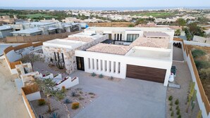 Un bâtiment moderne doté d’une cour intérieure, caractérisé par un mélange de matériaux de construction, notamment de la pierre et du béton, un garage et un jardin aménagé avec des cactus et de petits arbres.