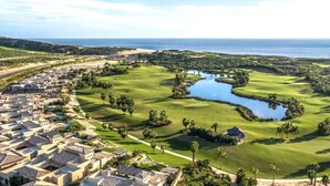 Un parcours de golf agrémenté d’un plan d’eau, entouré de bâtiments résidentiels et offrant une vue sur l’océan.