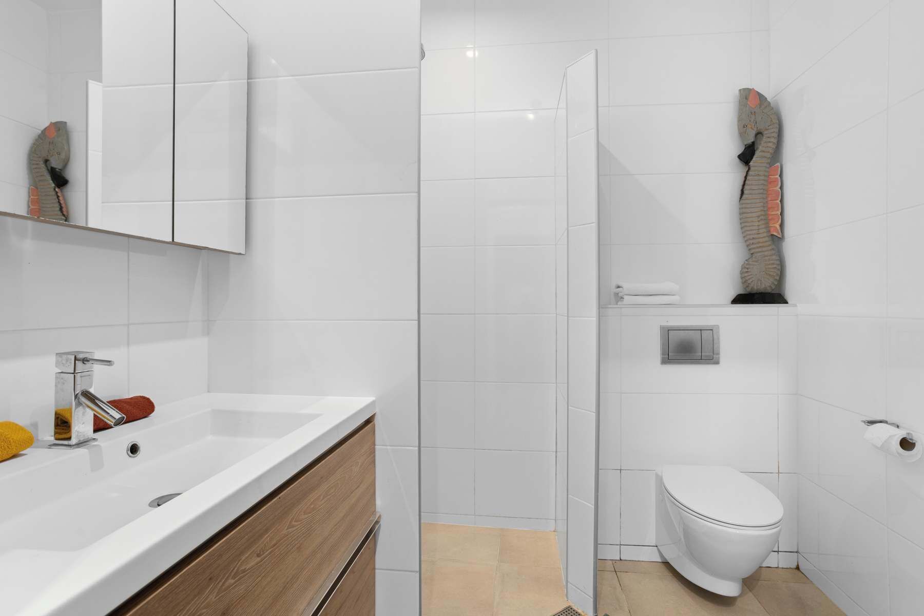 Ein modernes Badezimmer mit Waschbecken, Holzschrank, Duschkabine und Toilette.