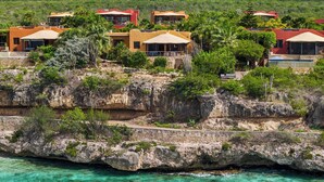 Un hotel a la costa amb diversos edificis, penya-segats rocosos i aigües turqueses cristal·lines.