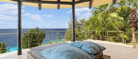 A bedroom with a view of the ocean, a wooden bed, and a balcony with a railing.