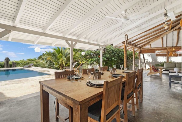 An outdoor dining area with a pool, wooden furniture, and a view of the ocean.