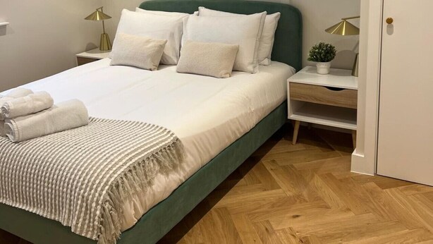 A modern bedroom with a green bed, white bedding, a small round window, a Bauhaus artwork, and a wooden herringbone floor. - Stylish London Bridge Apartment with Shard Views (london)