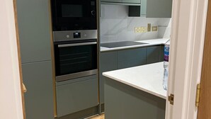 A compact kitchen with built-in appliances, a herringbone-patterned wooden floor, and a white countertop. - Stylish London Bridge Apartment with Shard Views (london)
