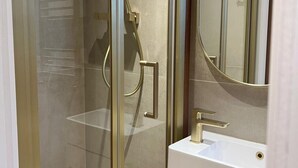 A modern bathroom with a glass shower enclosure, a white sink, and a large mirror. - Stylish London Bridge Apartment with Shard Views (london)