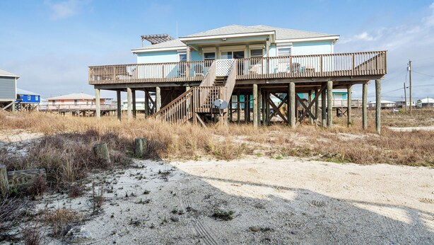 A beachfront house with a wooden deck and stairs leading to a balcony.