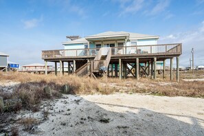 A beachfront house with a wooden deck and stairs leading to a balcony. - Beautiful Gulf View home on West End (Dauphin Island)