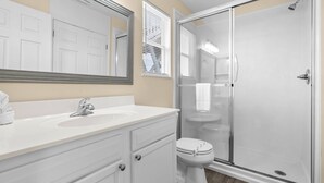 A bathroom with a white sink, mirror, and toilet, and a glass-enclosed shower area.