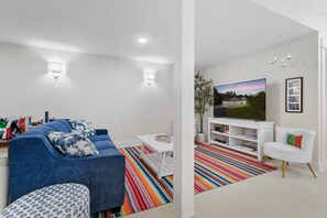 A modern living room with a blue sofa, white coffee table, and a colorful striped rug. - TLC Cottage in Leland - New- sleeps 12! (Leland)