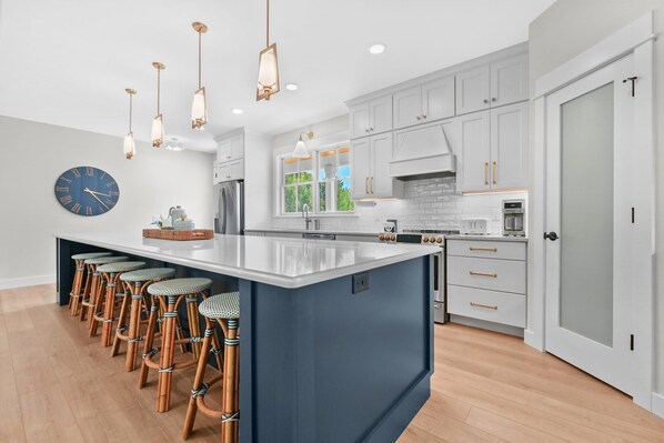 A modern kitchen with a large island, bar stools, and pendant lighting.