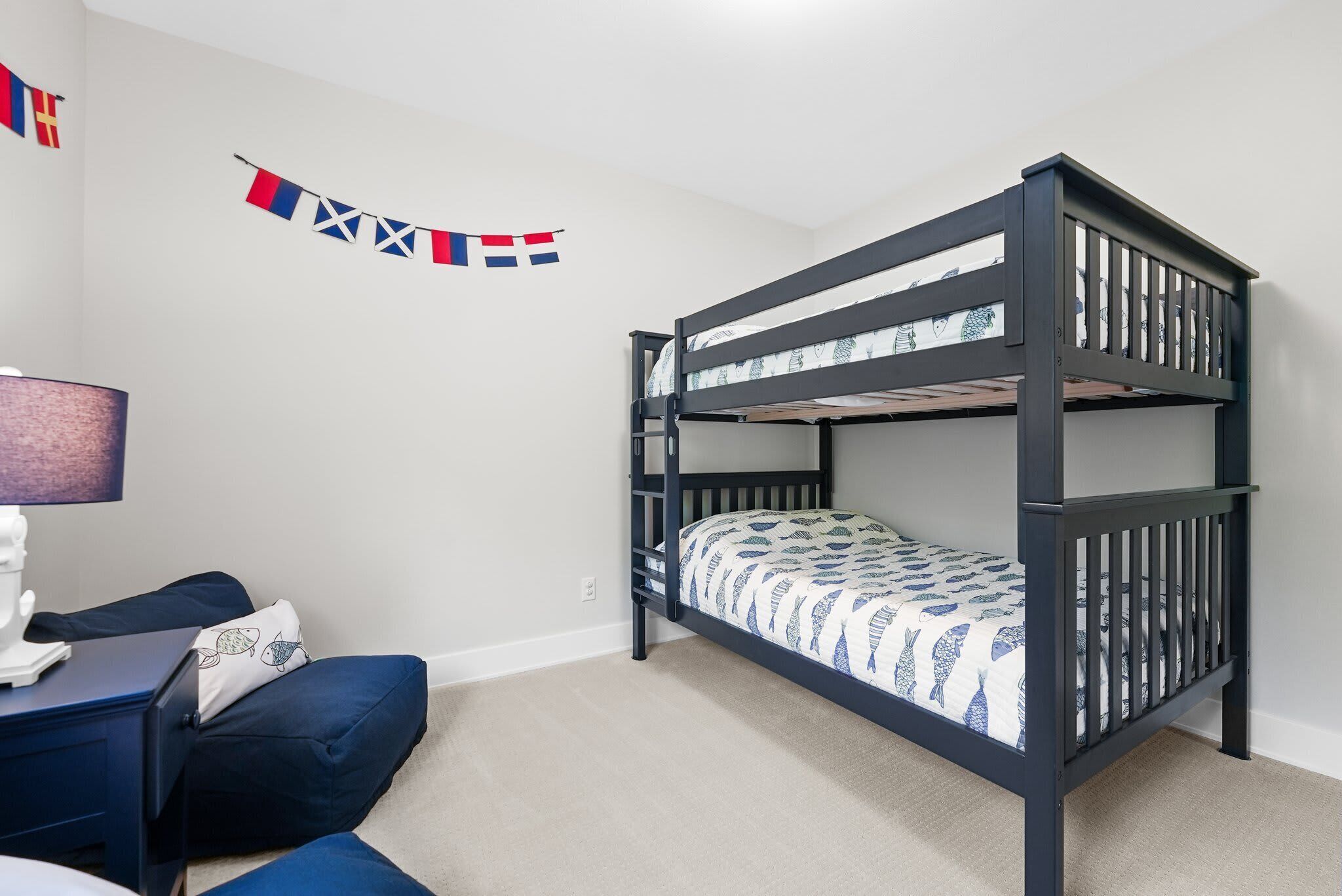 A bunk bed with a patterned bedspread, a desk with a lamp, and a wall-mounted flag.