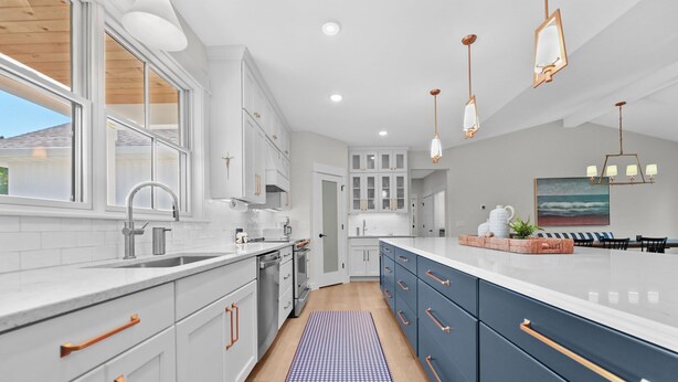 A modern kitchen with white cabinetry, a blue and white checkered rug, and a dining area with a view of the ocean.