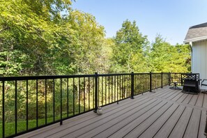 Um deck de madeira com guarda-corpo preto, cercado por árvores e um edifício.