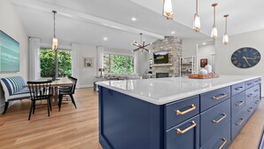 A modern kitchen with a large island, pendant lighting, and a stone fireplace.