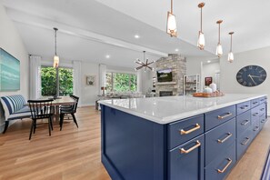 A modern kitchen with a large island, pendant lighting, and a stone fireplace. - TLC Cottage in Leland - New- sleeps 12! (Leland)
