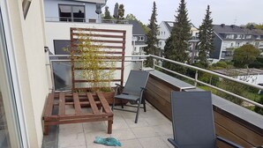 Un balcon avec une chaise en bois, une table et un pot de fleurs.
