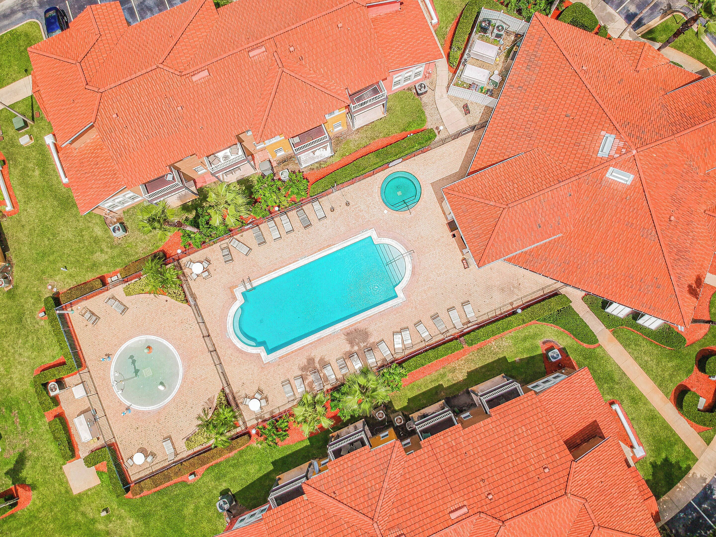 An aerial view of a property with a swimming pool, lounge areas, and a circular fountain.