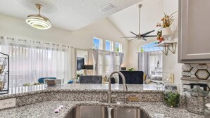 A kitchen with granite countertops, a double sink, a ceiling fan, and a view of the living area.