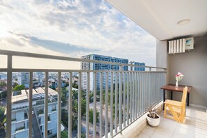 A balcony with a view of a cityscape, a potted plant, a wooden chair, and a table with a vase of flowers. - Gin House - Golden Mansion APT Phu Nhuan (Ho Chi Minh City)