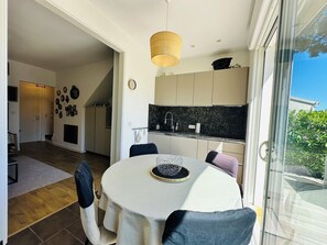 Un coin repas comprenant une table ronde, des chaises, un luminaire suspendu, ainsi qu’une cuisine équipée d’armoires et d’un plan de travail.