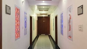 A hallway with patterned wall decorations, a wooden door at the end, and a light switch on the wall. - Maa Tara Homestay (Rishikesh)