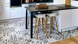 Uma cozinha moderna com armários brancos, uma ilha central com banquetas, micro-ondas, forno e luminárias pendentes.