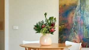Un comedor con una mesa redonda de madera, un florero y una silla blanca.