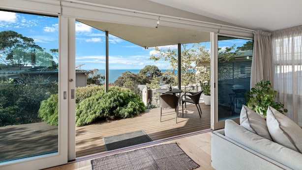 Una sala de estar moderna con un ventanal corredizo que da a una terraza con vistas al océano.