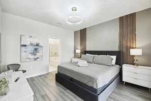 Ein modernes Schlafzimmer mit einem großen Bett, Nachttischen, einem Schreibtisch und einem durch eine offene Tür einsehbaren Badezimmer.