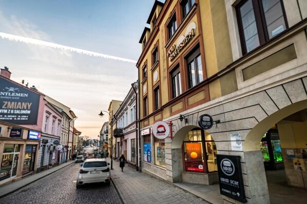 A street view with buildings, a car, and a pedestrian. - Pod Ratuszem (Rzeszów)