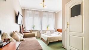 A hotel room with a bed, a sofa, a desk with a computer, and a window with sheer curtains. - Pod Ratuszem (Rzeszów)