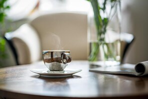 A cup of coffee on a saucer, a newspaper, and a vase with green plants on a table.