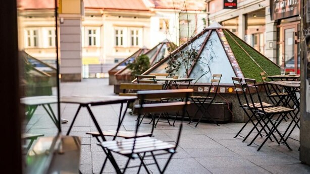 An outdoor café with tables and chairs, a small garden area, and buildings in the background. - Pod Ratuszem (Rzeszów)