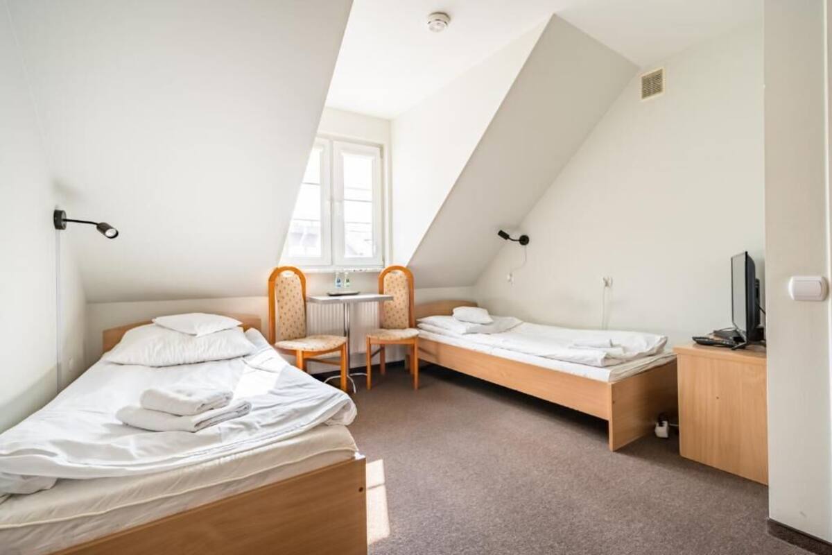 A small, well-lit room with two single beds, a desk, and a chair.