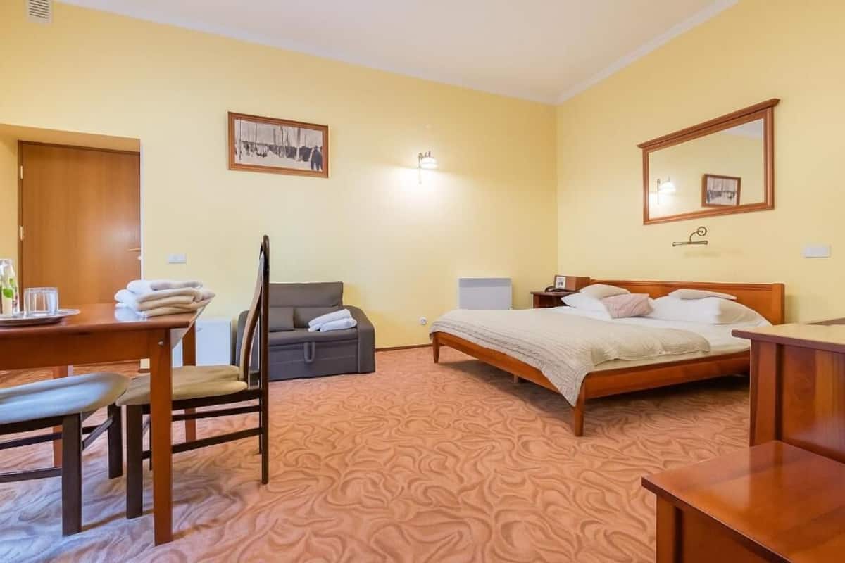 A hotel room with a bed, a desk, a chair, a sofa, a mirror, and a picture on the wall.