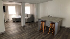 Un espacio habitable moderno y abierto, con zona de cocina, sofá y mesa con taburetes.