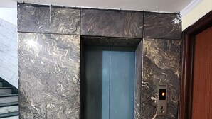 An elevator with a marble wall, a digital display, and a wooden door. - Hotel Mid Town (New Delhi)