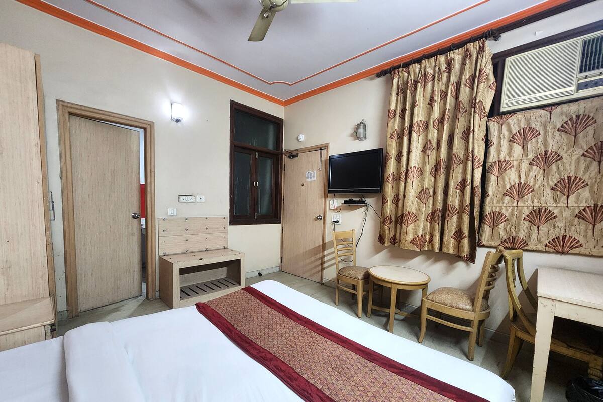A hotel room with a bed, a desk, a chair, a television, and a window with curtains.