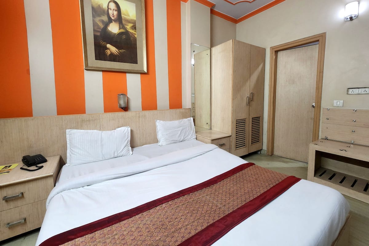 A hotel room with a bed, a wardrobe, a mirror, and a painting on the wall.