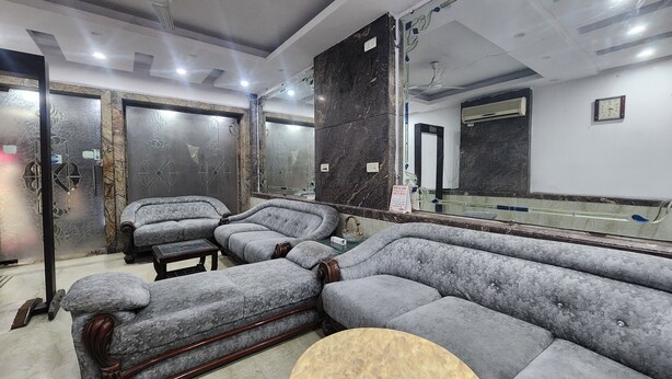 A modern living room with a sectional sofa, a round coffee table, and a large mirror. - Hotel Mid Town (New Delhi)