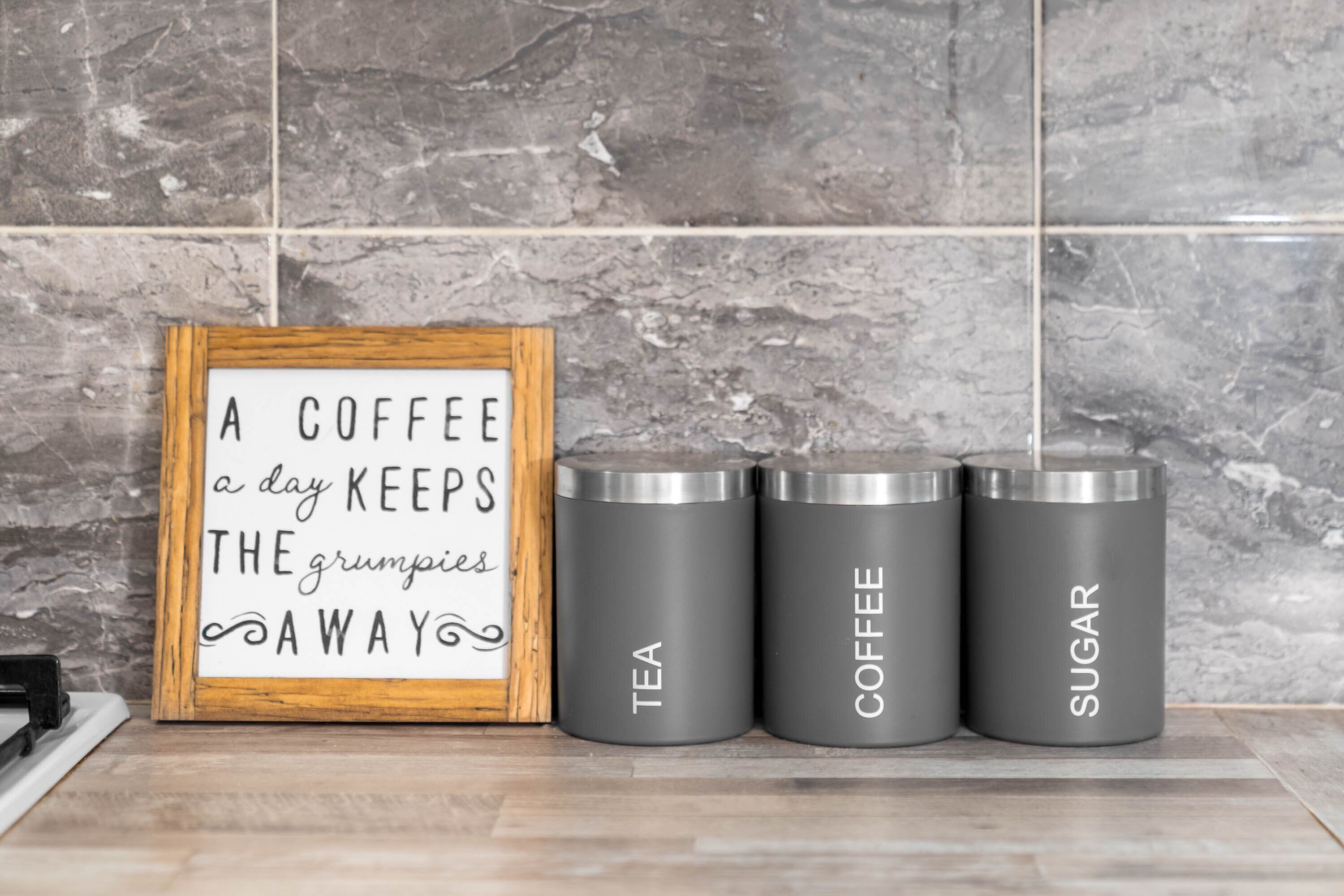 A kitchen counter with a framed sign and three stainless steel containers labeled tea, coffee, and sugar.