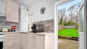Een moderne keuken met witte kasten, een koffiehoek en uitzicht op een groen gazon door een glazen deur.