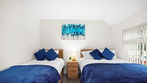 Een tweepersoonskamer met twee bedden, elk voorzien van blauw beddengoed, een nachtkastje met een lamp, en een blauw abstract schilderij aan de muur.