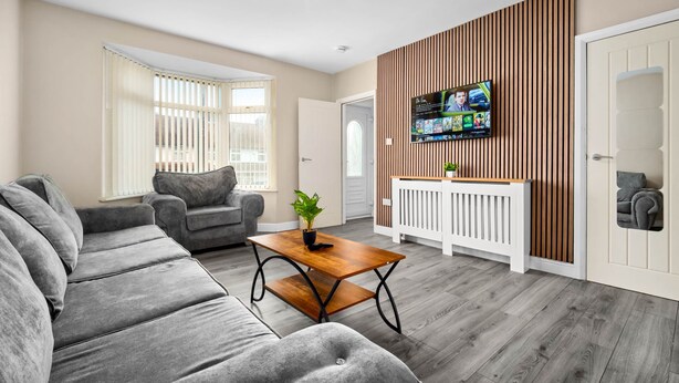 Een moderne woonkamer met een grijze hoekbank, een houten salontafel en een televisie bevestigd aan een houten wand.