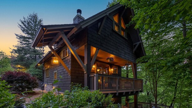 A wooden cabin with a porch, surrounded by lush greenery.