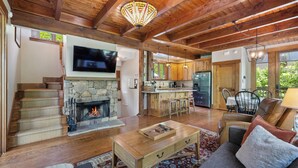 A spacious living room with a stone fireplace, wooden ceiling beams, a flat-screen TV, and a cozy seating area with a sofa and ottoman.