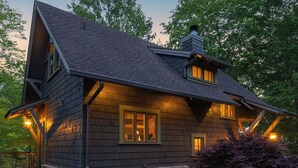 A rustic cabin with a steeply pitched roof, stone foundation, and a gravel driveway.