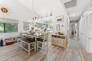A modern kitchen with a dining area, wooden flooring, and a view of the outdoors.