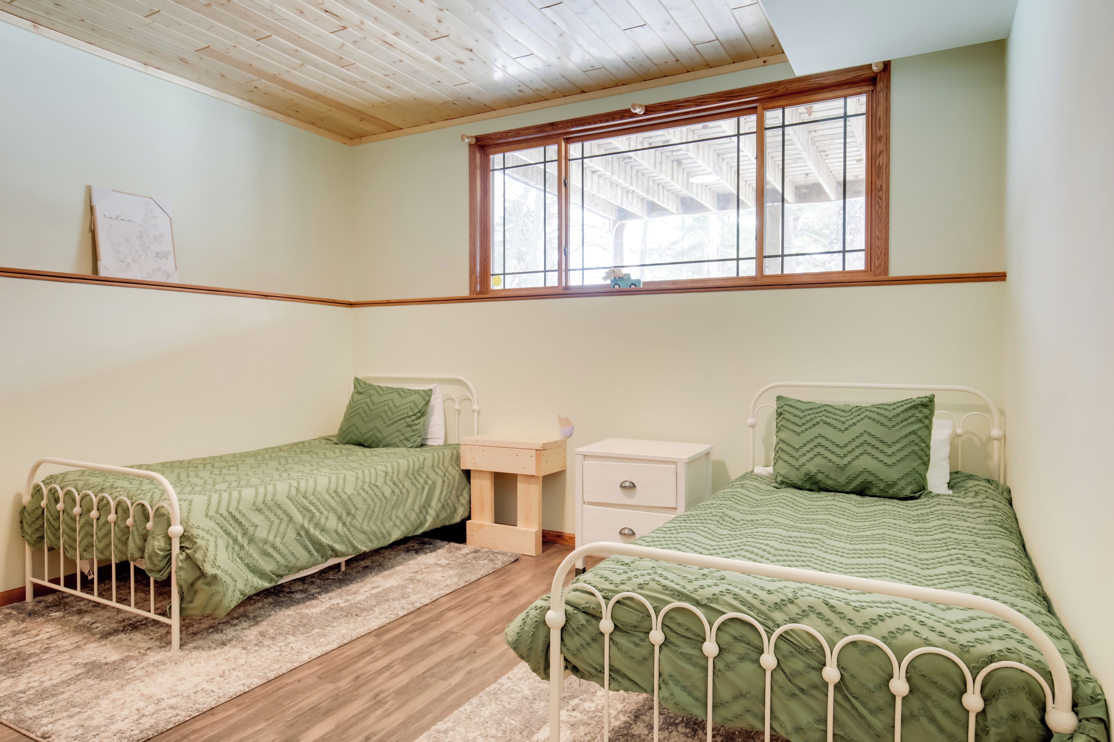 A bedroom with two single beds, a wooden headboard, a window with a view, a small bedside table, and a nightstand.